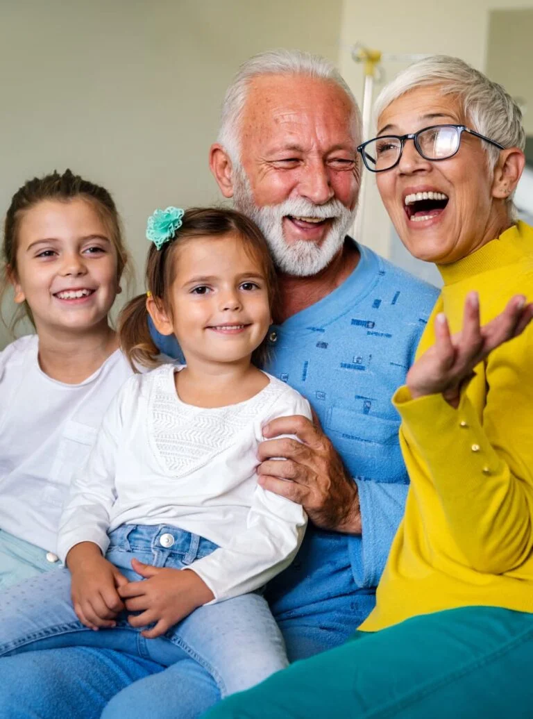 Un groupe de personnes âgées riant avec leurs enfants sur un canapé.