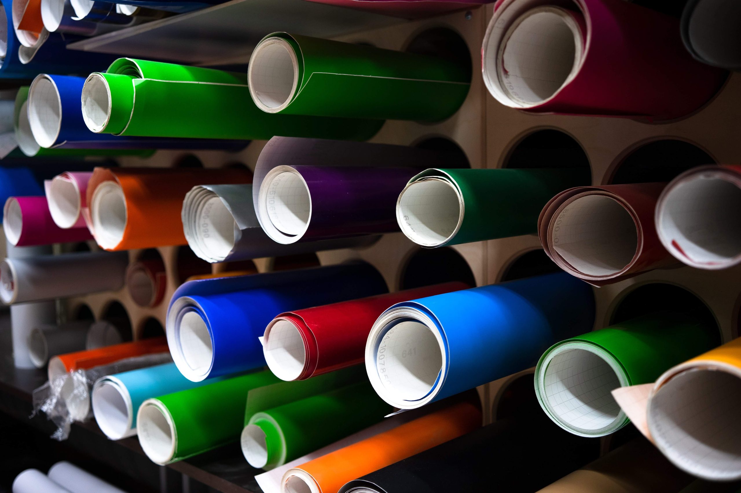 Étagère avec plusieurs rouleaux de vinyle adhésif coloré, organisée pour une utilisation dans la signalisation.