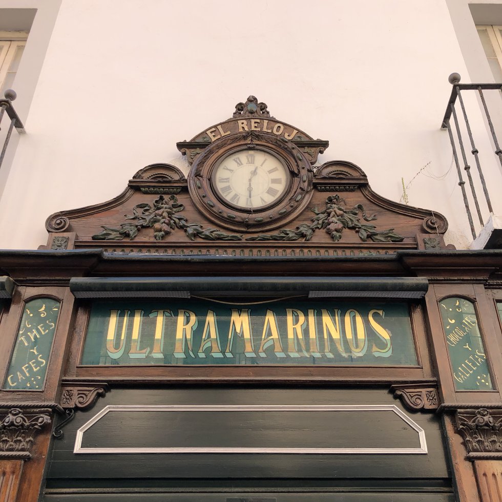Placa histórica de "ULTRAMARINOS" na fachada de El Reloj (Calle Arfe, Sevilha), parte da identidade gráfica urbana.