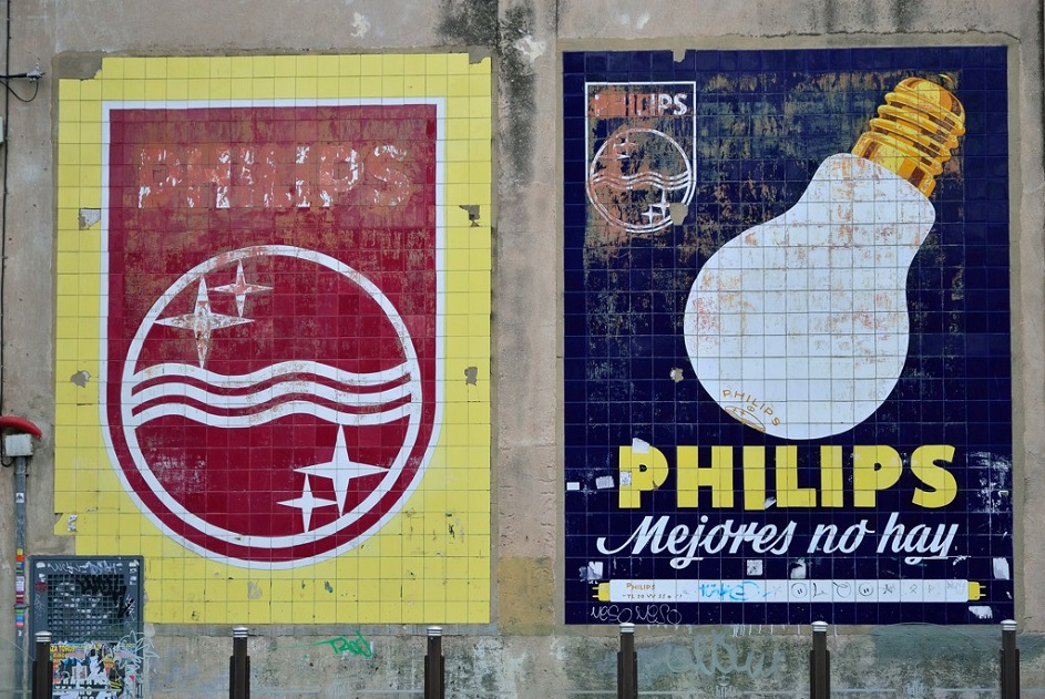 Painel publicitário em cerâmica Philips com uma lâmpada e o texto "PHILIPS Não há melhor", ao lado de outro painel com o logótipo, na Rua Blanquerías em Valência, identidade gráfica urbana