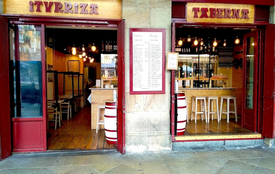 Fachada da Taberna Iturriza na Plaza Nueva, Bilbau, com os letreiros "ITURRIZA" e "TABERNA" nas portas, um exemplo de identidade gráfica urbana.