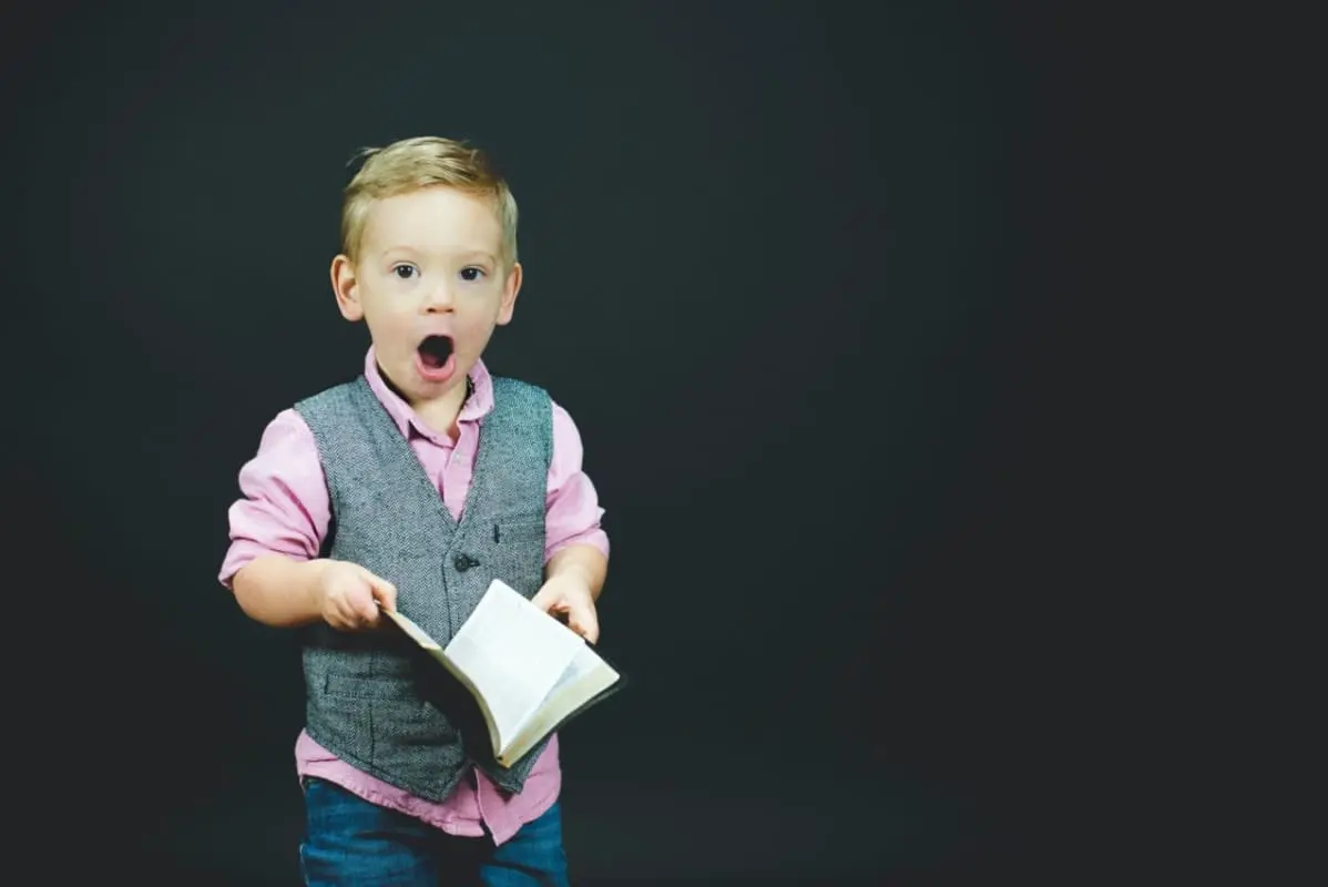 Niño con chaleco gris y camisa de vestir rosa sosteniendo un libro