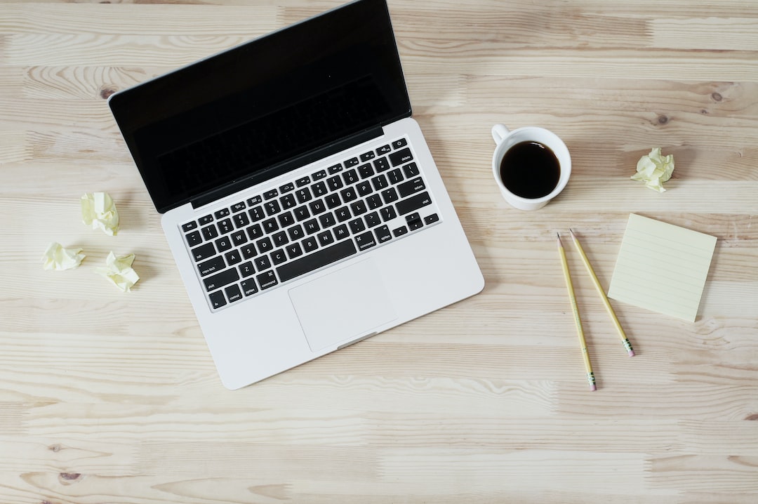 A laptop on a wooden table with a cup of coffee and a notepad.