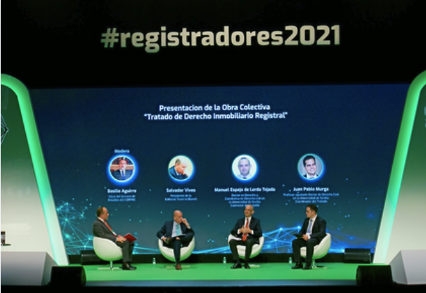 Cuatro hombres se sientan en un escenario decorado en verde y negro bajo un cartel que reza #registradores2021 en el Congreso Registradores. Detrás de ellos, una pantalla muestra sus nombres y el título Tratado de Derecho Inmobiliario Registral.