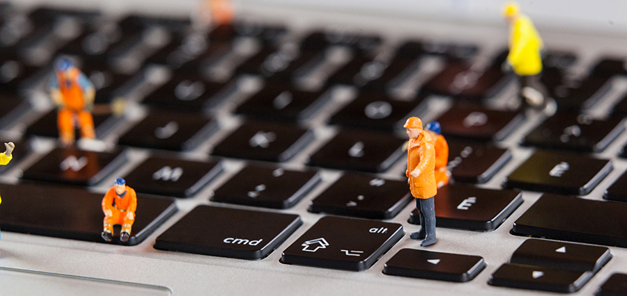 Miniature construction workers on a laptop keyboard.