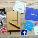 A notebook, pen, and social media stickers on a wooden table.