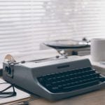 A typewriter and a cup of coffee occupy a desk.