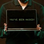 A man holding a laptop displaying an alert message indicating a successful WordPress attack.