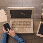 Amelia is multitasking with her laptop and mobile phone on a wooden table.