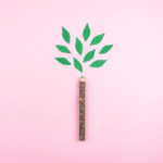 A pencil with a green leaf showing its low carbon footprint on a bright pink background.