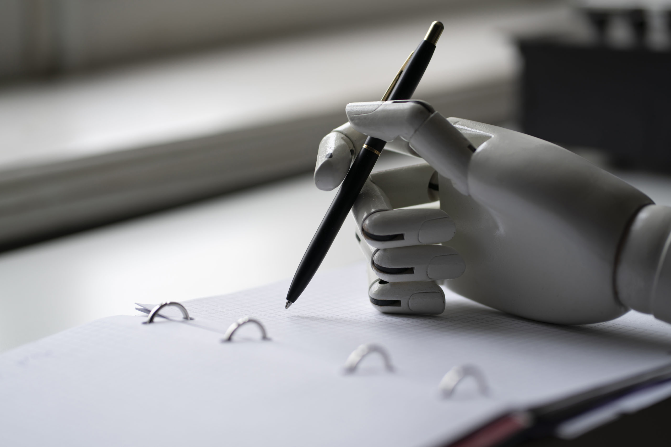 A robot's hand writing on a notepad with a pen.